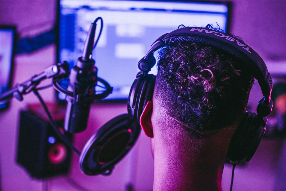 Image of a young man with headphones sitting in front of a microphone and computer