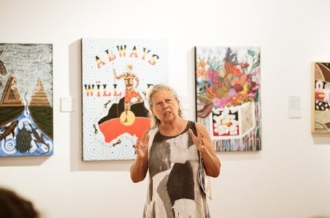 An image of a woman standing in front of two First Nations Artists works of art.